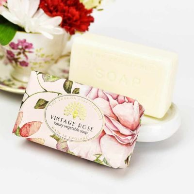 A soap bar on a soap dish with another wrapped bar in front. The wrapping has a rose pattern on it and says "Vintage Rose."