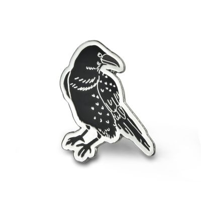 A black metal enamelled pin badge in the shape of a raven. 