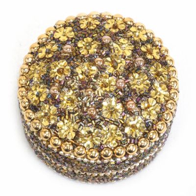 A small beaded trinket box tin with a golden flower pattern on the lid. 