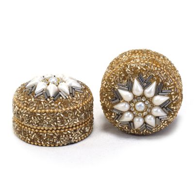 A gold and pearl beaded trinket box with a flower pattern on the lid. 