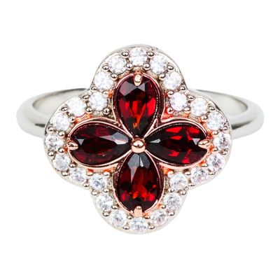 A silver ring with a quatrefoil pendant inlaid with four pear0cut red garnets and surrounded by 20 clear topaz gemstones. 