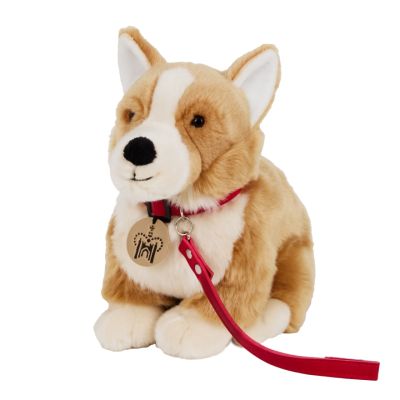 A soft Cogi dog plush toy in cream and light-brown fur. With black bead eyes and a soft black nose. It has a red collar and leash with a metal dog tag featuring the Historic Royal Palaces logo. 