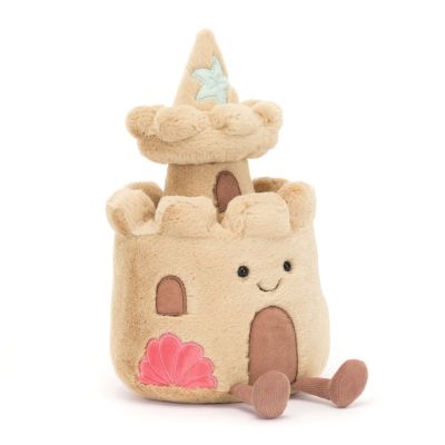 A light-beige coloured Jellycat plush toy in the shape of a sandcastle with a pointy turret. The sandcastle has a brown door and window with brown dangly legs. There is an embroidered smile and hard eyes. 