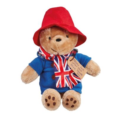 A Paddington Bear soft toy wearing a red hat and blue duffle coat with a union jack patterned scarf around his neck. 
