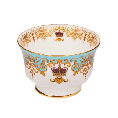 A round, white sugar bowl with a small pedestal base with gold rim details and a blue, gold and burgundy pattern including ornate details and a royal crown. 