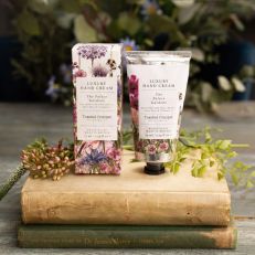 A tube of hand cream with a white sticker label with illustrated flowers in pinks and green, next to a cardboard box also with the same illustration of flowers on it. Both are on top of an old book and there are sprigs of flowers behind.