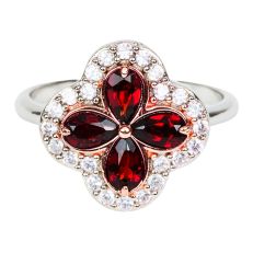 A silver ring with a quatrefoil pendant inlaid with four pear0cut red garnets and surrounded by 20 clear topaz gemstones. 