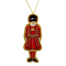 A red and gold embroidered hanging decoration of a Yeoman Warder from the Tower of London. Wearing a black hat and traditional red uniform with a gold crown on the chest. 