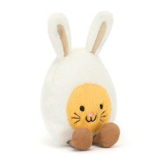 A soft plush Jellycat toy in the shape of an egg with bunny ears. The egg yolk in the centre has an embroidered smiling bunny face with whiskers.