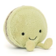 A round plush soft toy in the shape of a green macaron. With a smiley face and dangly legs. 
