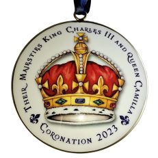 A round, white, metal hanging decoration with a crown illustration in the centre and 'their majesties King Charles III and Queen Camilla coronation 2023' text