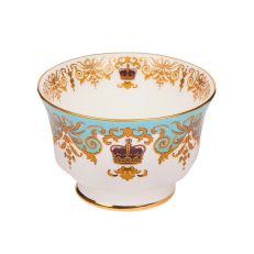 A round, white sugar bowl with a small pedestal base with gold rim details and a blue, gold and burgundy pattern including ornate details and a royal crown. 
